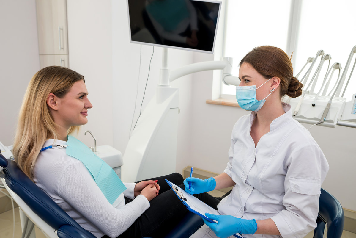 She is sitting in the dentist's chair. The dentist explains and advises the patient.